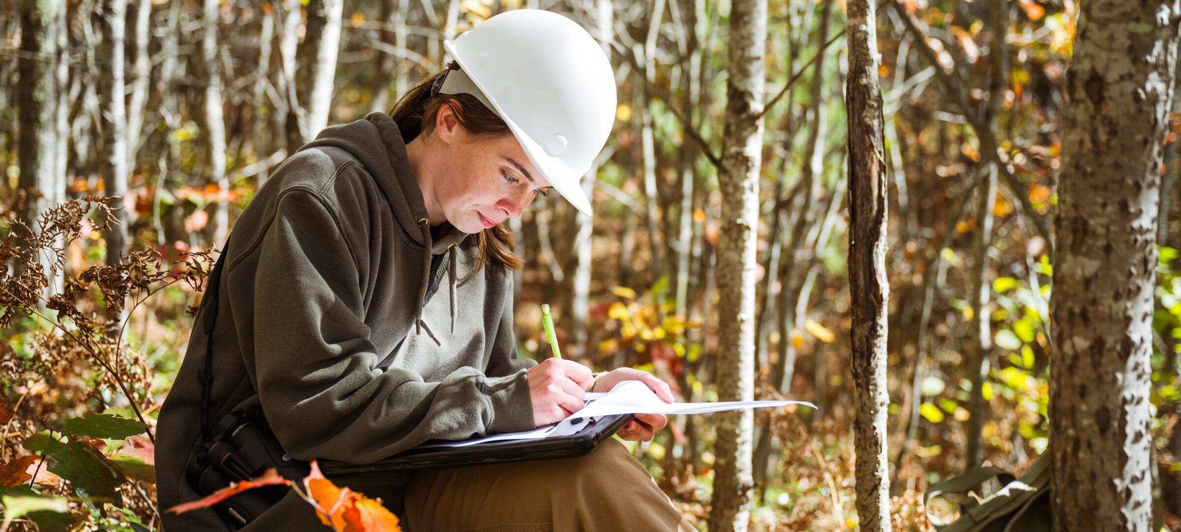 A student writing on a pad of paper in the woods