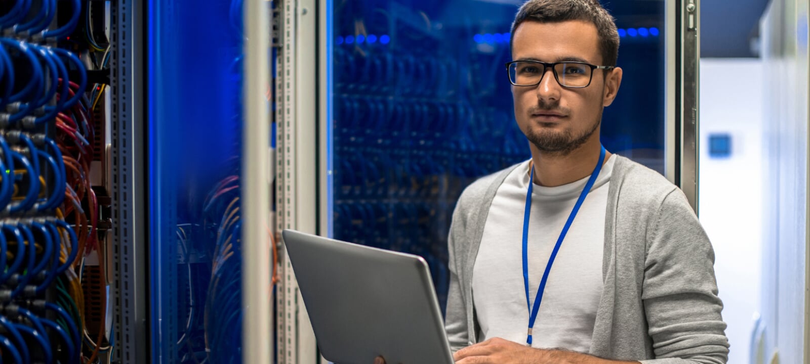 Young male computer engineer with a laptop standing in front of a mainframe.