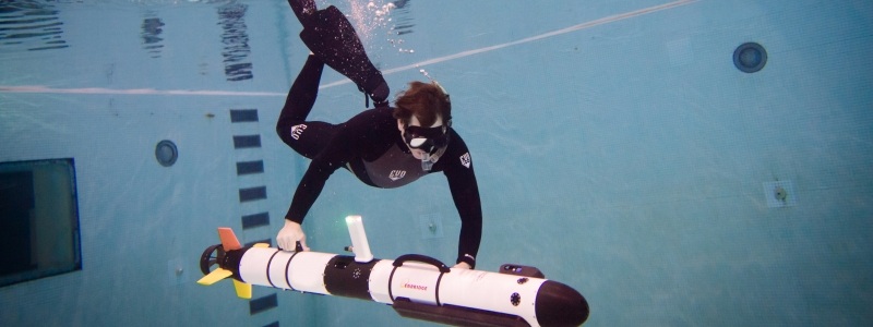 A diver in an indoor pool adjusts an underwater sonar device.