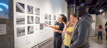 Three gallery attendees observe a collection of nine black and white microscopic images in the Rozsa’s A-Gallery.