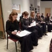 Seated choral performers in performance dress attire reviewing music before a performance in the Choral Rehearsal Room.