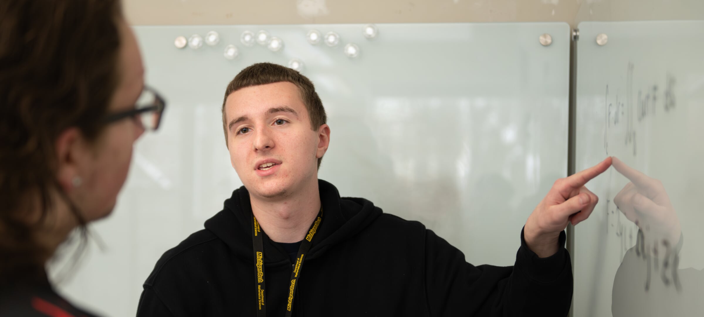 Mathematics students pointing to board, explaining.