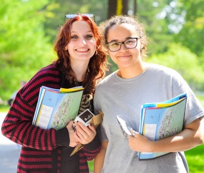 Students smiling next to each other holding books