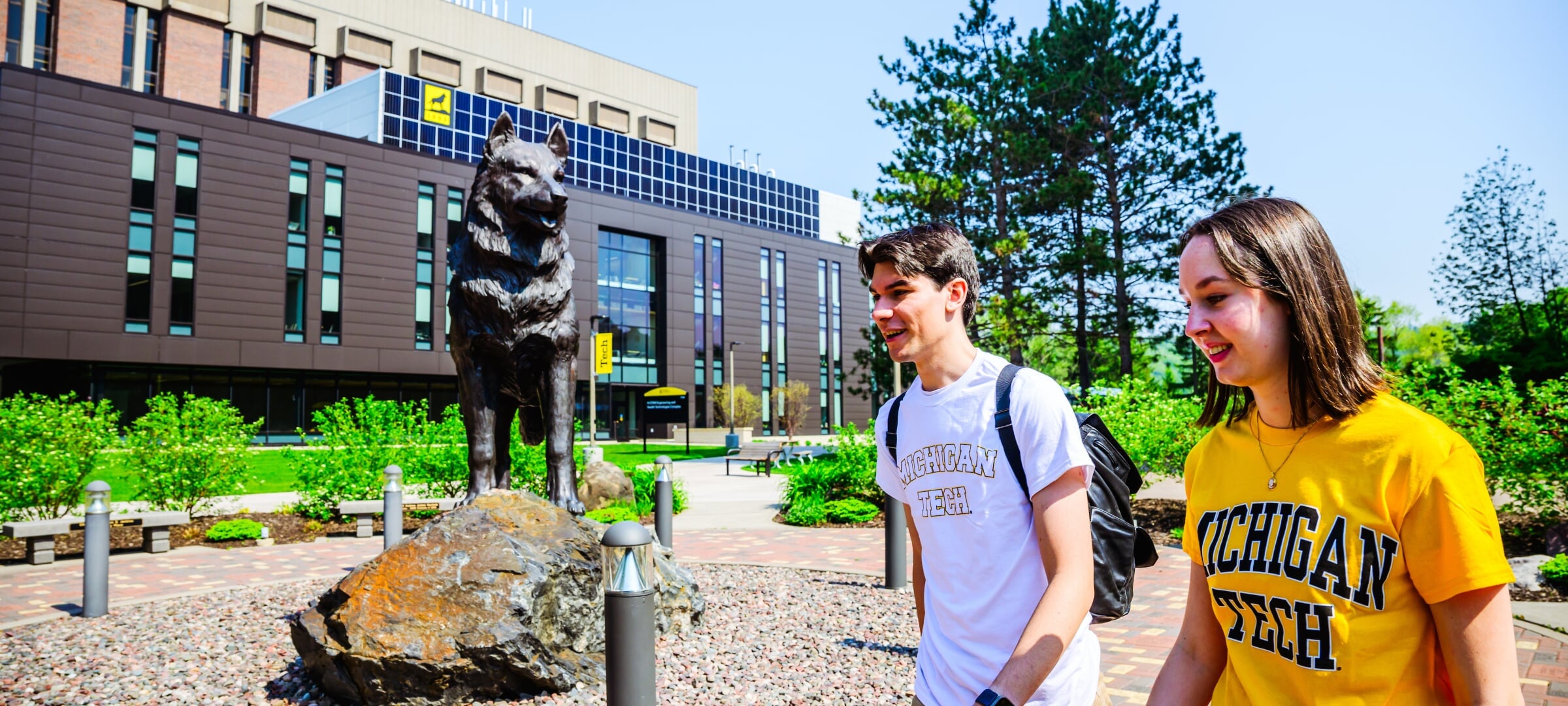 Two students walking next to the Husky Statue on Michigan Tech's campus.