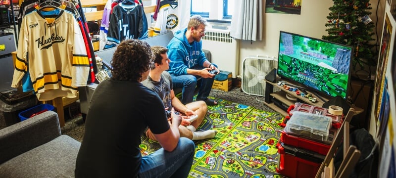 Three students playing a videogame console in a residence hall room