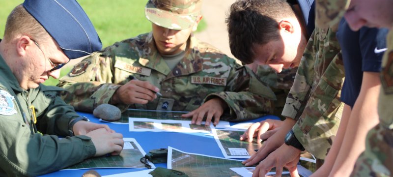 Seated cadets in uniform watch cadets in dress uniforms give a rifle demonstration