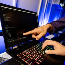 finger pointing to computer screen while another hand is on the keyboard