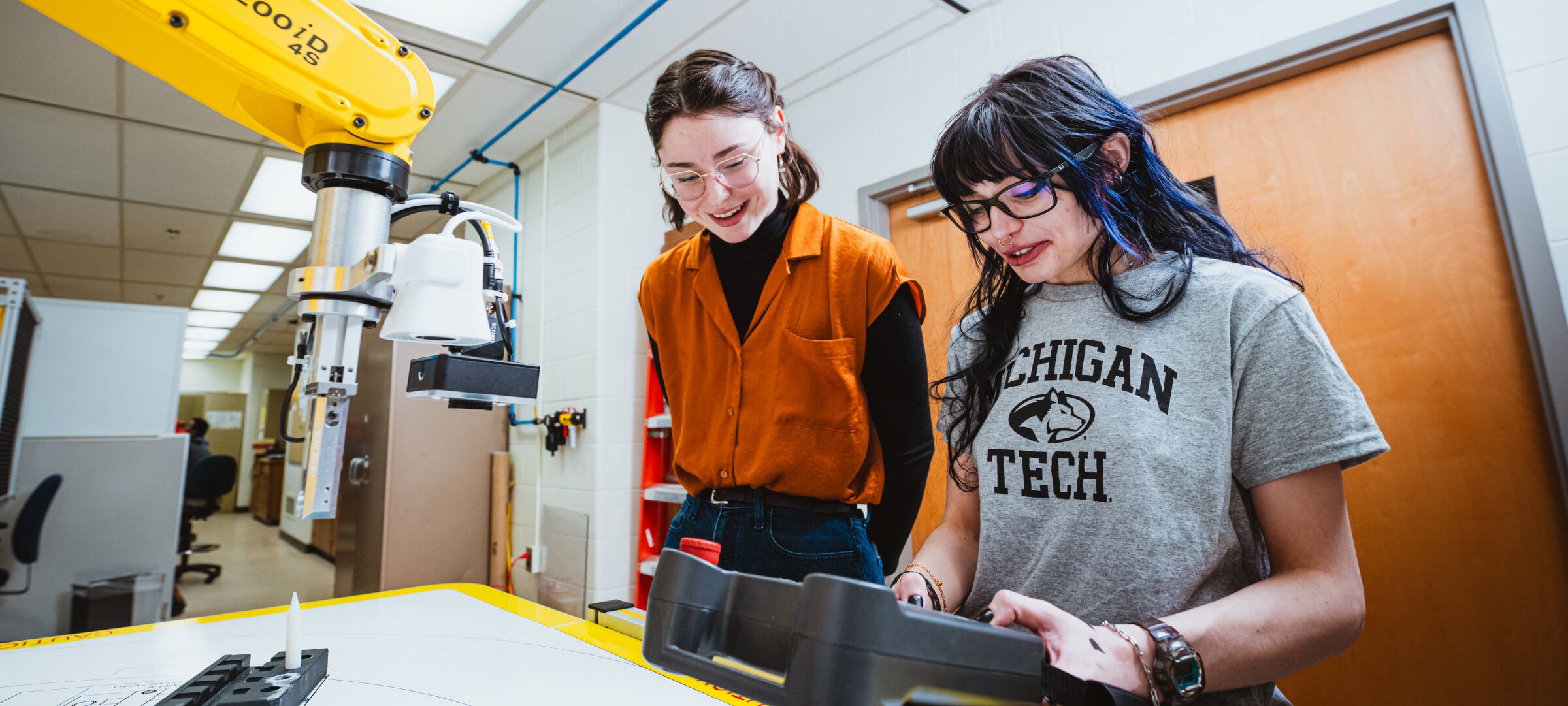 Two students, one operating robotics, the other looking on