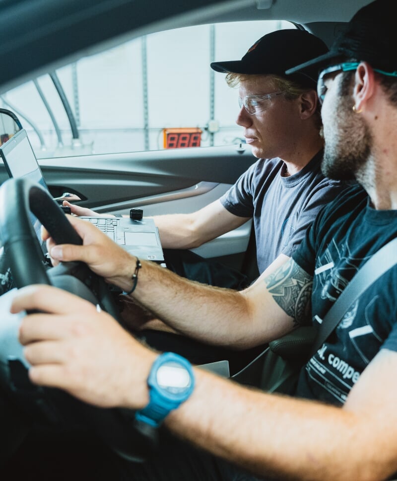 2 people sitting in a parked car looking at a computer