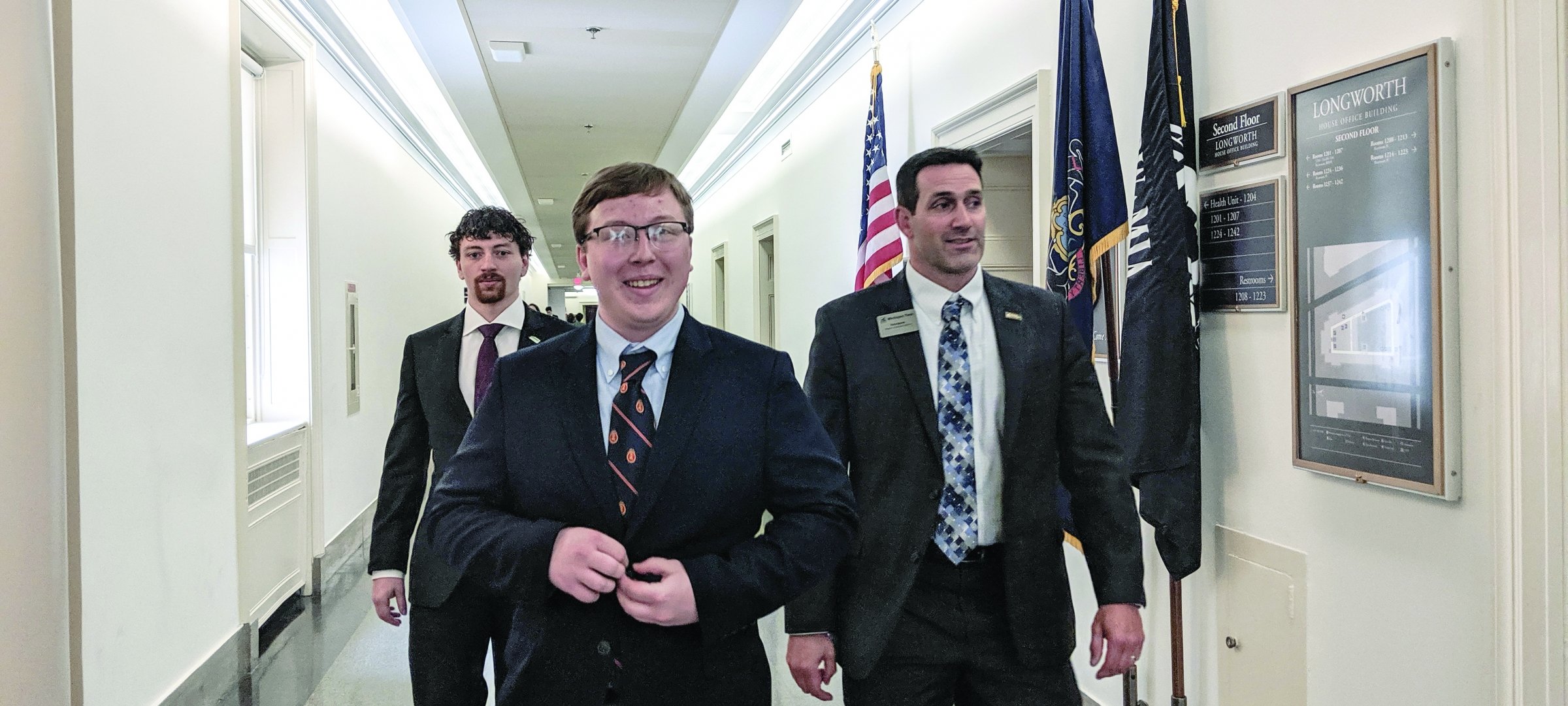 Three men wearing suits walking down a hallway.