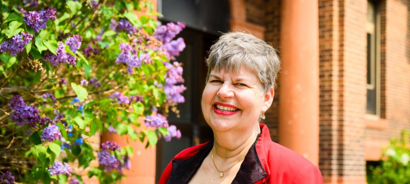 Marie Cleveland, standing in front of a blooming lilac tree outside the Academic Office Building.