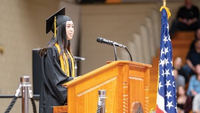 Aerith Cruz in her cap and gown standing at a podium with a microphone.