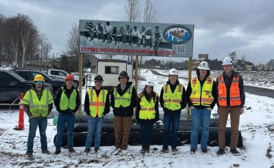 Eight people in bright vests and hard hats stand in front of a sign saying Future Home of Ironworkers Local 8.