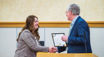 Sydney Lurvey shaking hands with Dan Green as he hands her a certificate.