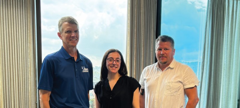 Three people who serve the community stand in front of windows as their contributions are celebrated.