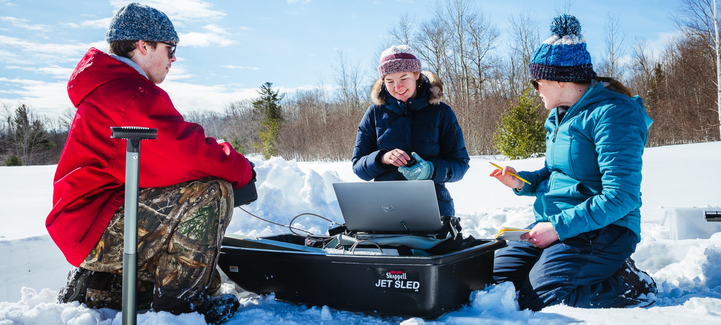 students doing research in the snow with a laptop sitting on a sled