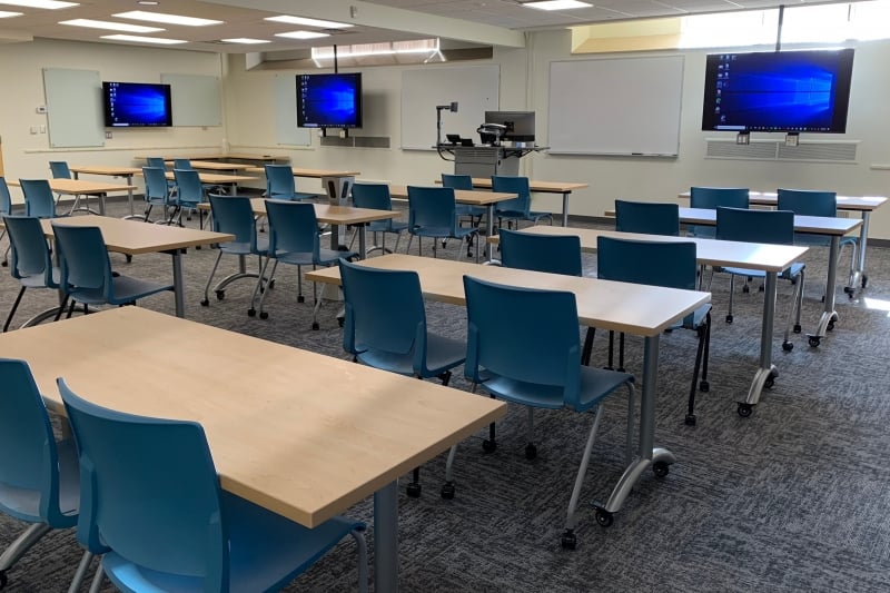 Wads G42 showing 14 short rectangular tables, each with 2 chairs, facing a wall with alternating whiteboards and monitors.