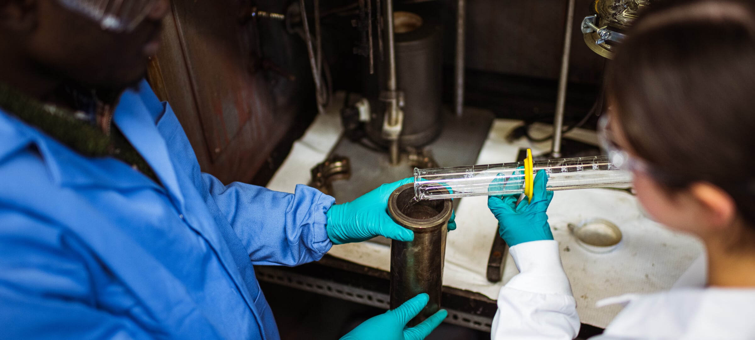 Two people pouring liquid out of graduated cylinder