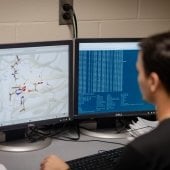 Researcher sitting looking at chemical formula simulation on a desktop.