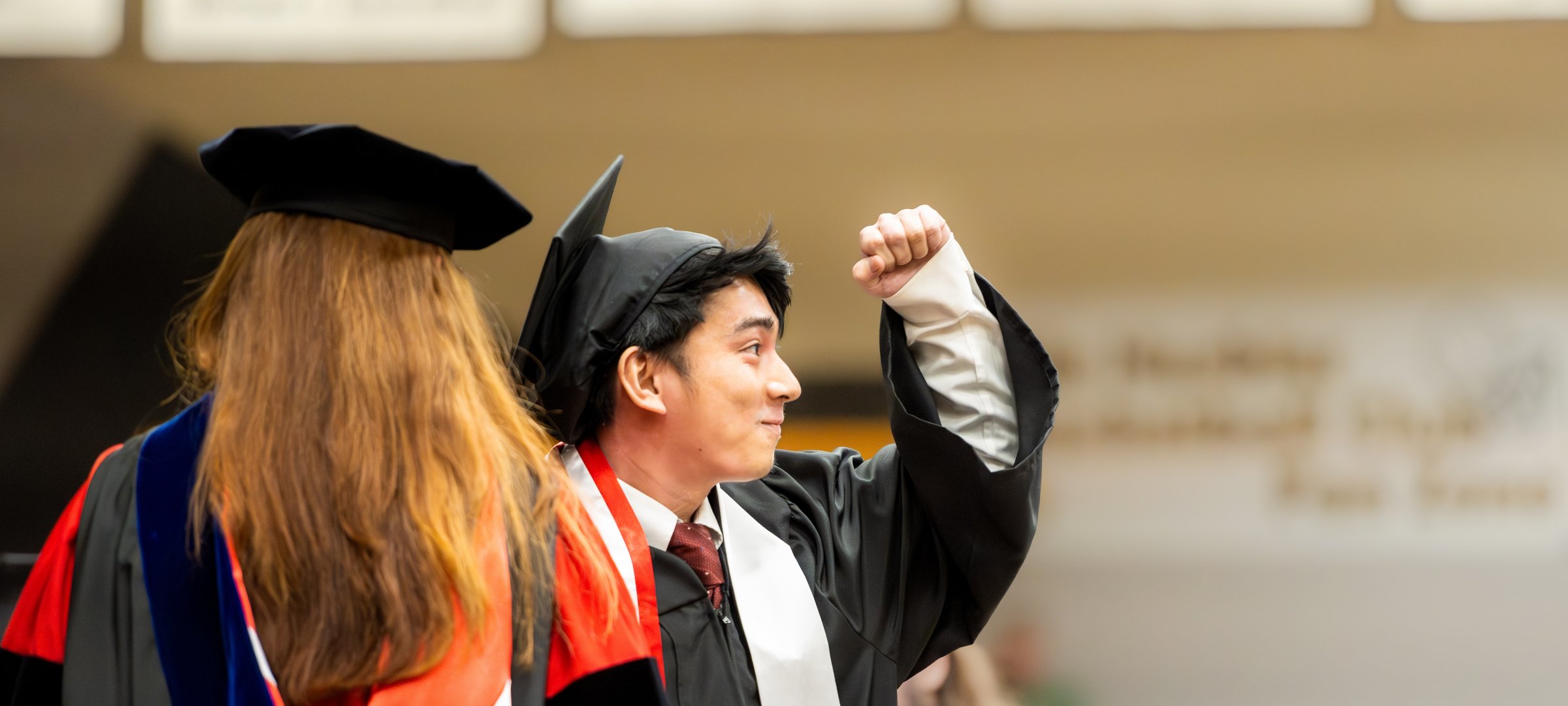 Student receiving degree and throwing a fist in the air while looking at the crowd.