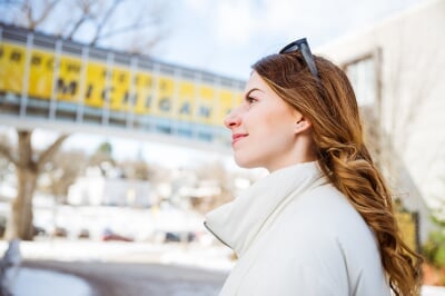 A young woman smiles in front of a sign outside on campus that says tomorrow needs Michigan Tech