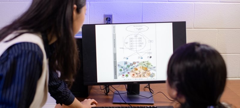 A faculty member and student view a cybersecurity image on a computer