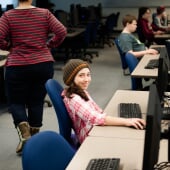 Young students sitting at computers while an instructor walks behind them