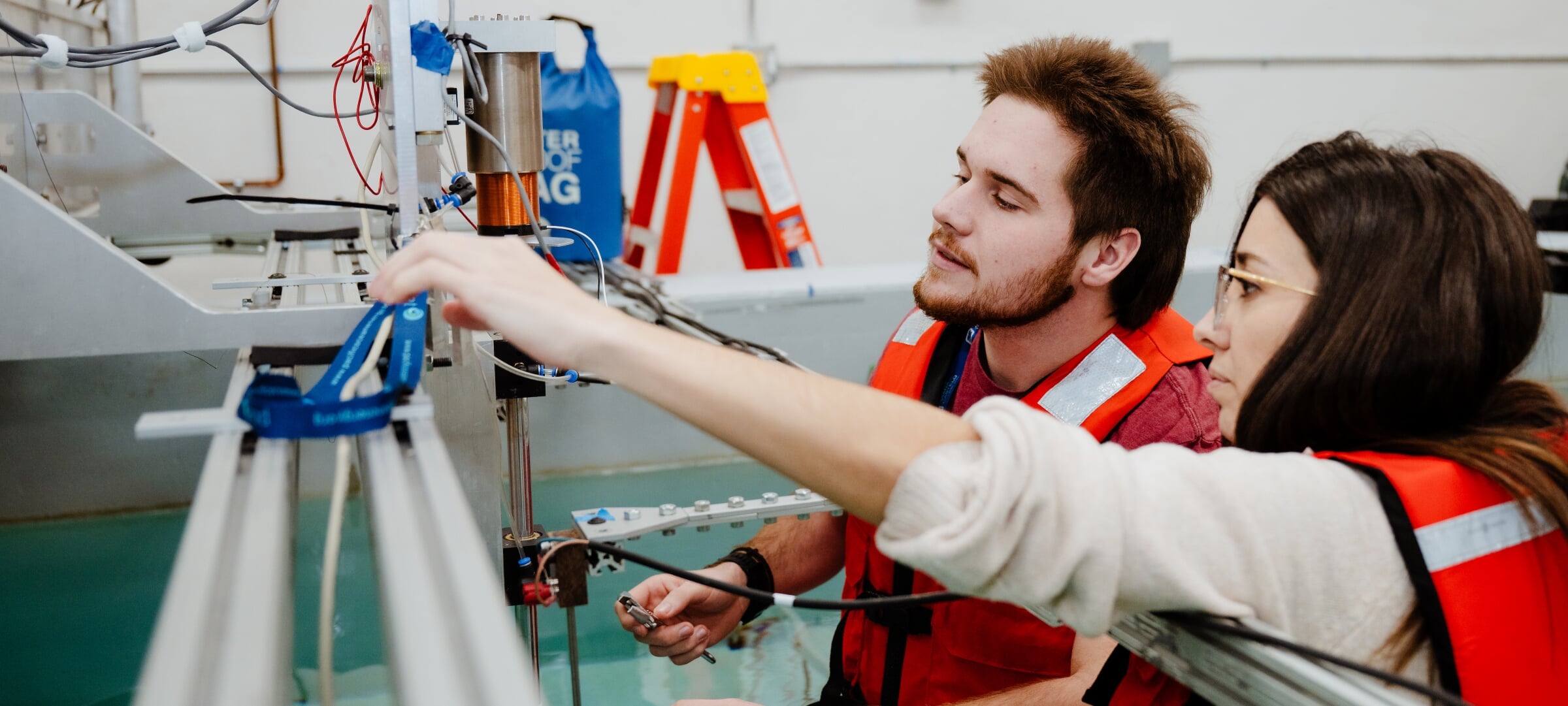 Two students in high visibility vests in a pool of water looking at a tool they are using