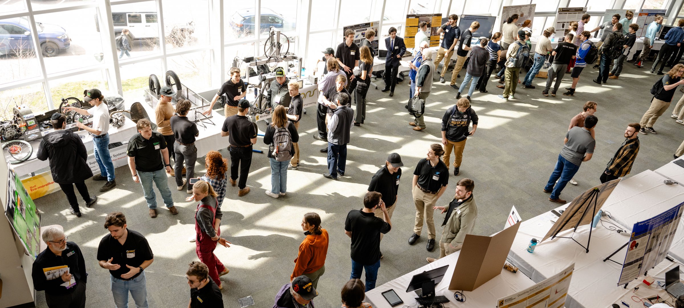 Design Expo — view of the design expo featuring students standing next to their displays setup on tables in rows