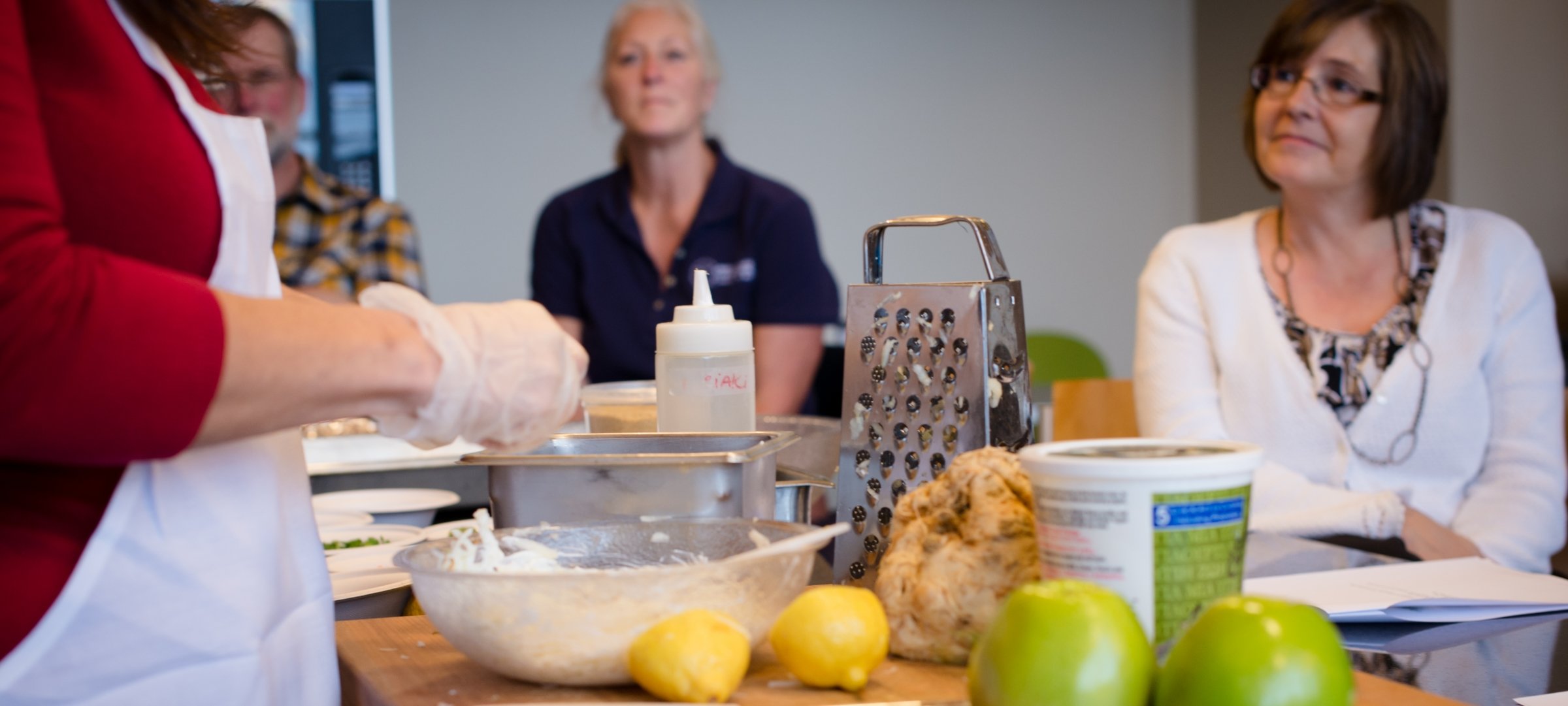 Someone preparing food at a table where others sit.