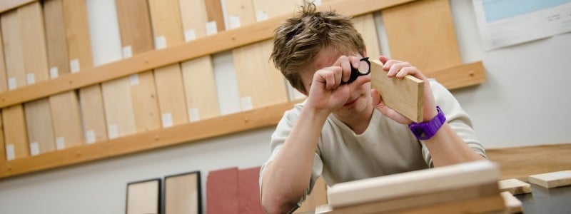 Student looking at a piece of wood with a magnifying glass.