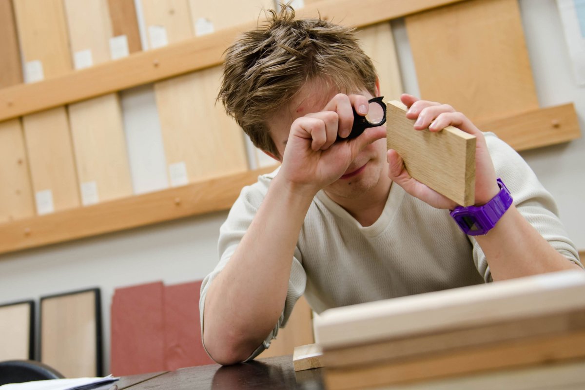 Student looking at a piece of wood with a magnifying glass.