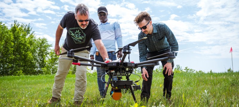 Three researchers looking at a drone on the ground in a field.