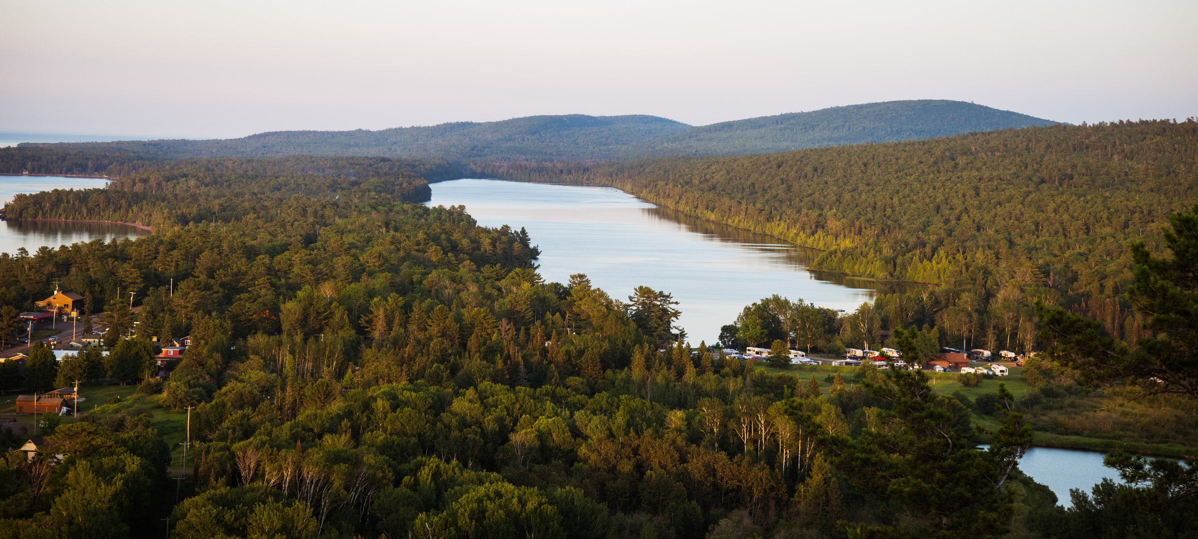 An aerial view of a forest with lakes, small clusters of houses, and large hills in the background..