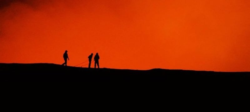 Silhouettes of three people with a bright red-orange background of a volcano.