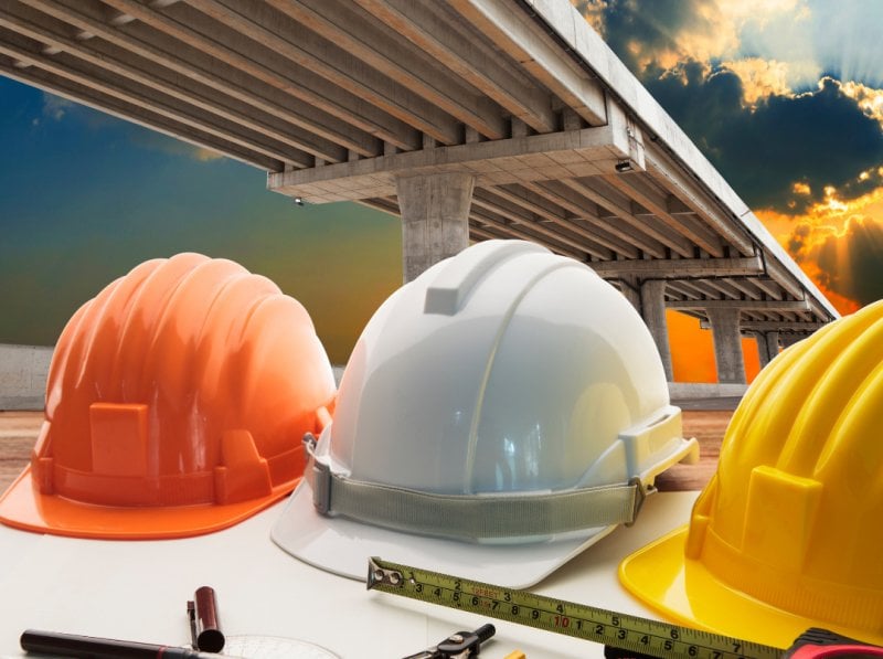 Three hard hats in the foreground with a bridge and a troubled blue sky in the background.