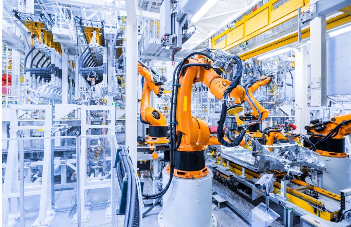 An orange robotic arm on the factory floor working.