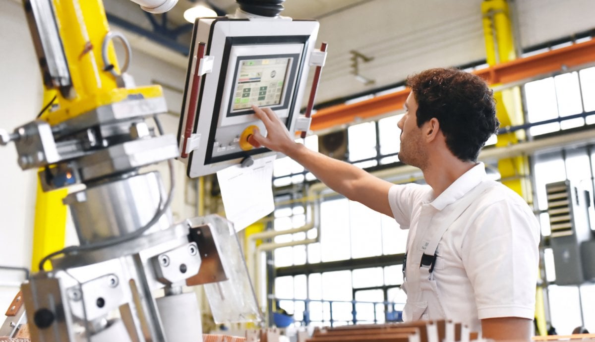 Young engineer punches code into a computer terminal in front of a manufacturing device.