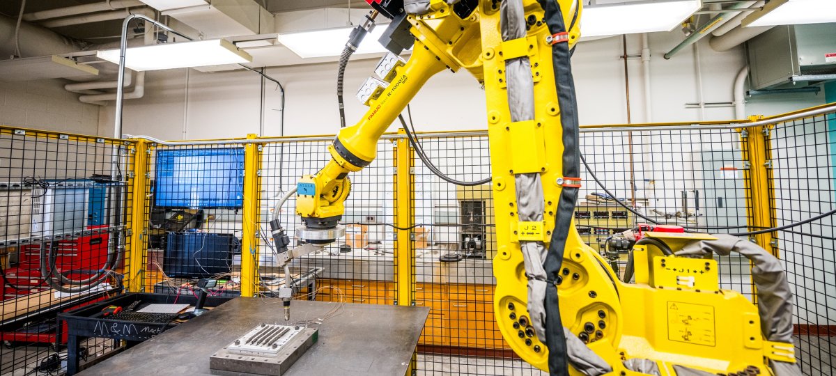 A large yellow robot prints metal in a manufacturing engineering setting.