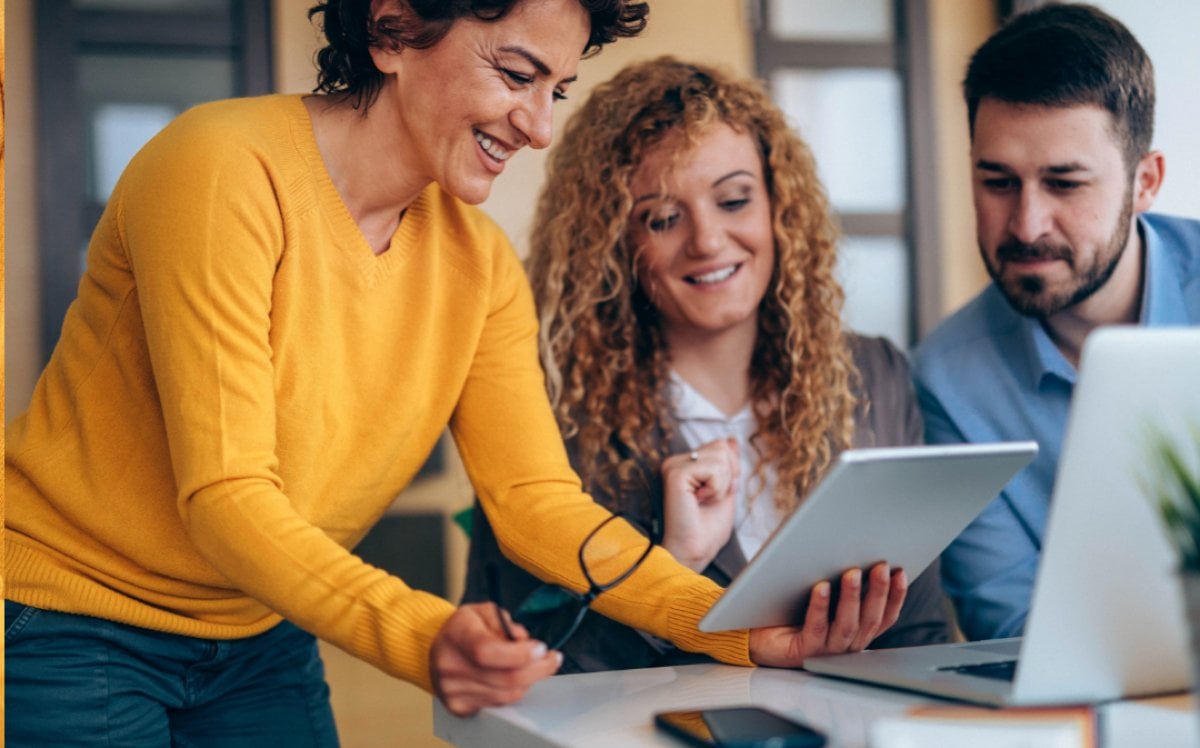 Three business professionals sitting around a table looking at a tablet.