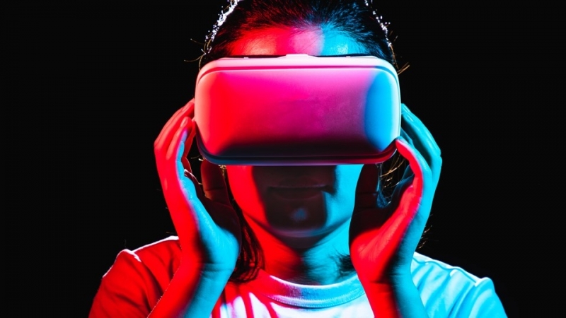 Woman wearing a virtual reality headset, looking straight ahead against a dark background.