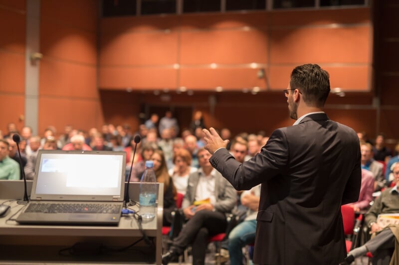 A man giving a public lecture in a room.