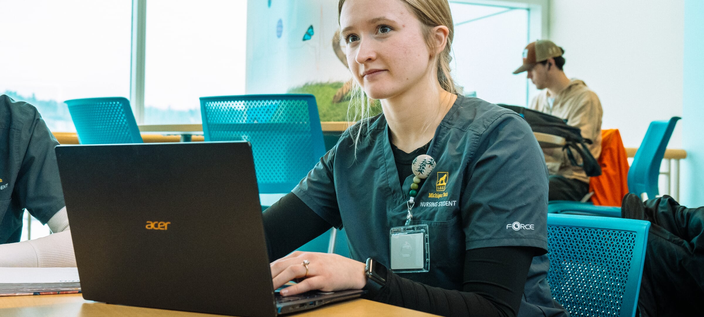 A graduate nursing student sits at a table with a laptop.