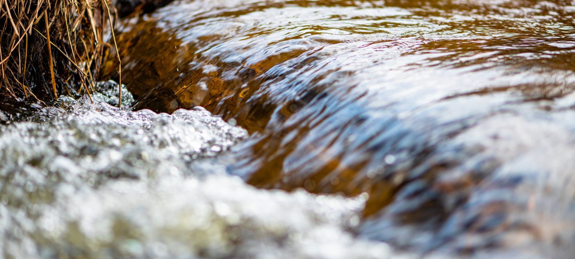 Extreme close-up of water rushing over a small drop, forming a tiny waterfall.