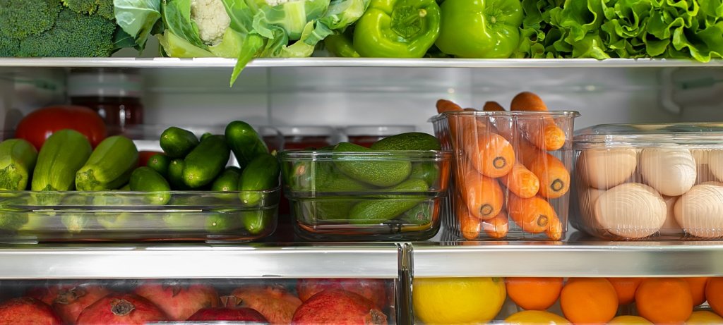 Fruits and vegetables in clear bins inside of a well-lit refrigerator