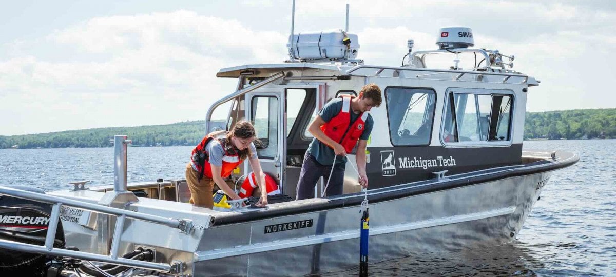 The RV Soliton floats on the water with two student researchers deploying a remotely operated vehicle (ROV)