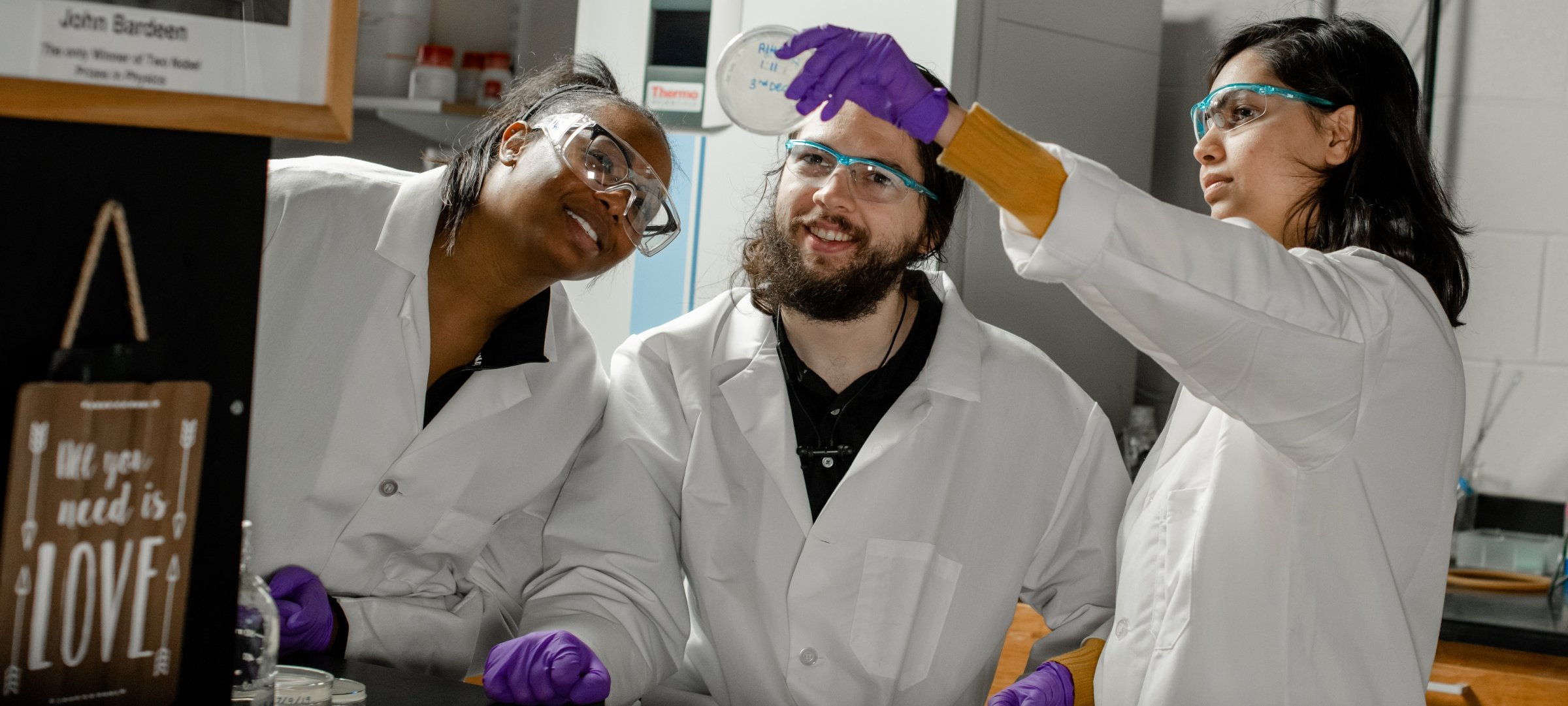 Three students looking at a petri dish being held up.