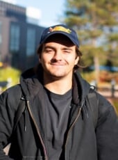Student, Pietrino, in a hat and jacket standing outside smiling