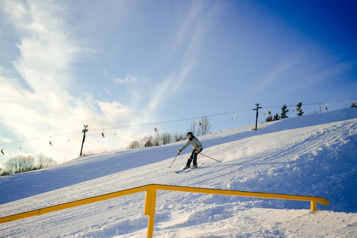 Huskies ski and snowboard for free at Mont Ripley, our very own hill that overlooks campus. Person skiing down a hill with a chairlift in the background.
