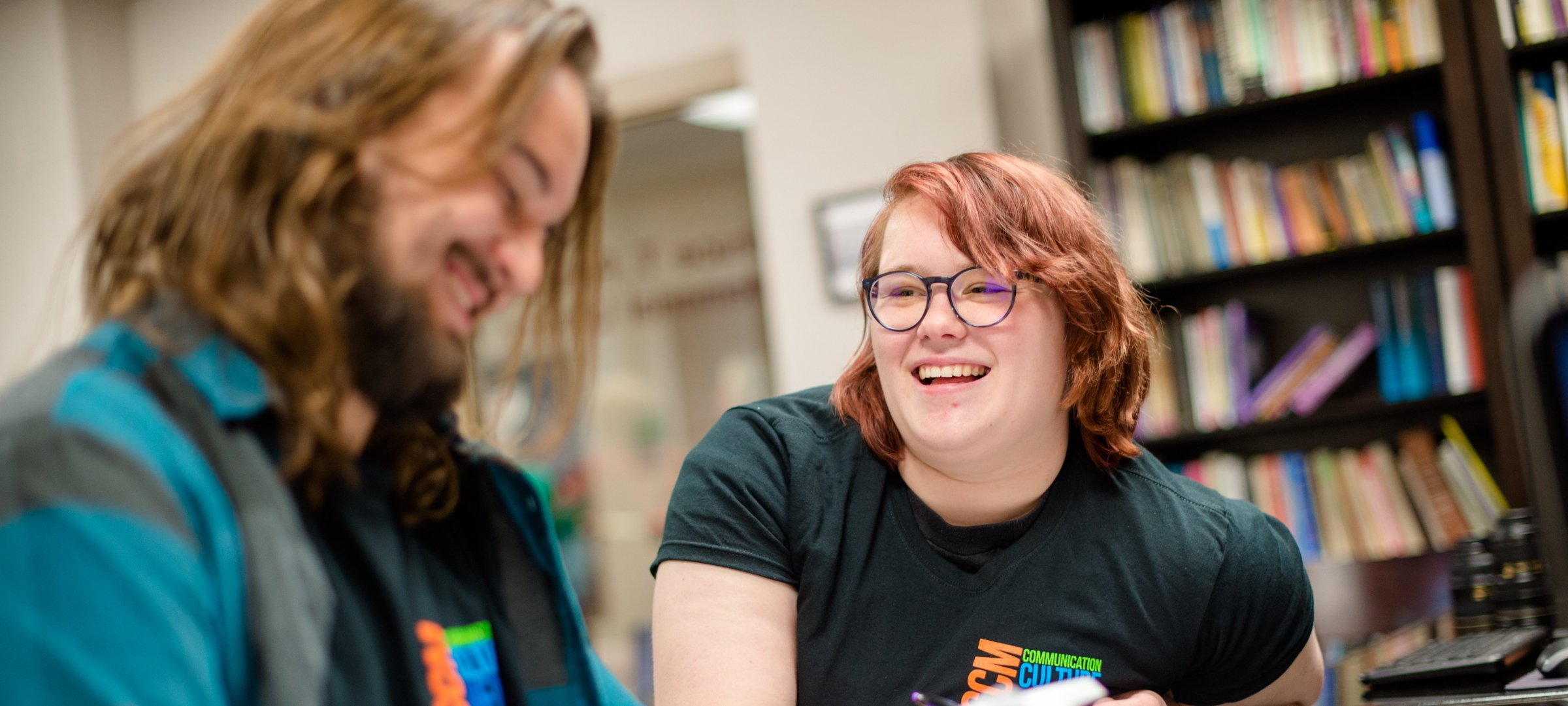 Two students sitting and laughing in the library of the Humanities department.